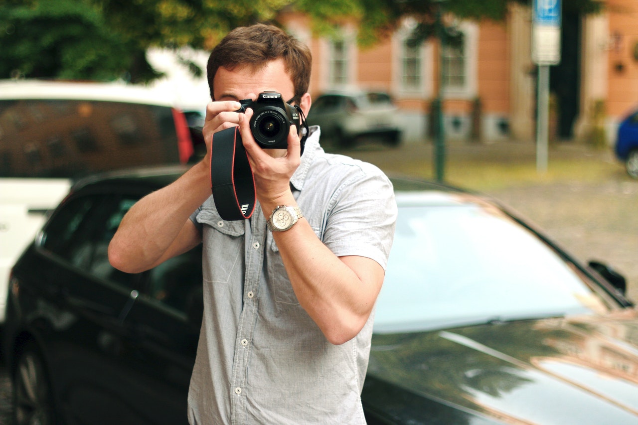 a boy holding camera in front of black car